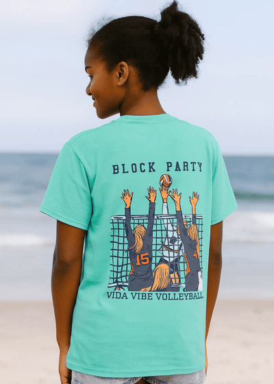 Child wearing a teal t-shirt with 'Block Party' and volleyball design on a beach.